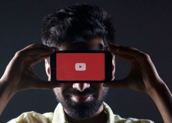 Chico con la cara tapada con un móvil que tiene YouTube